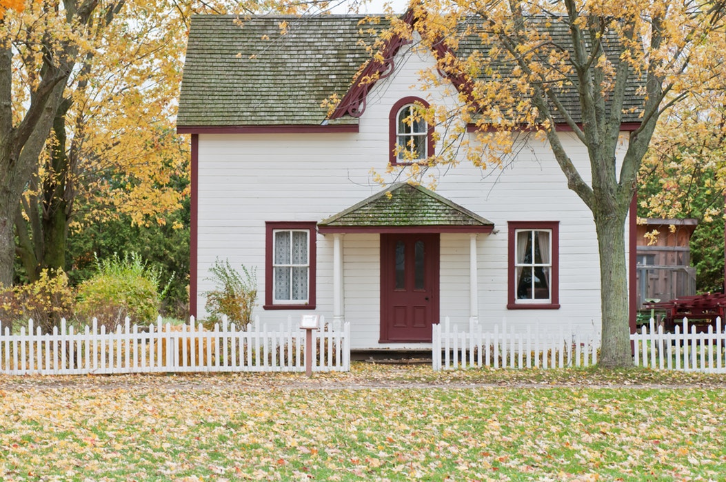 photo of a bungalow house surrounded by trees, white wooden fence