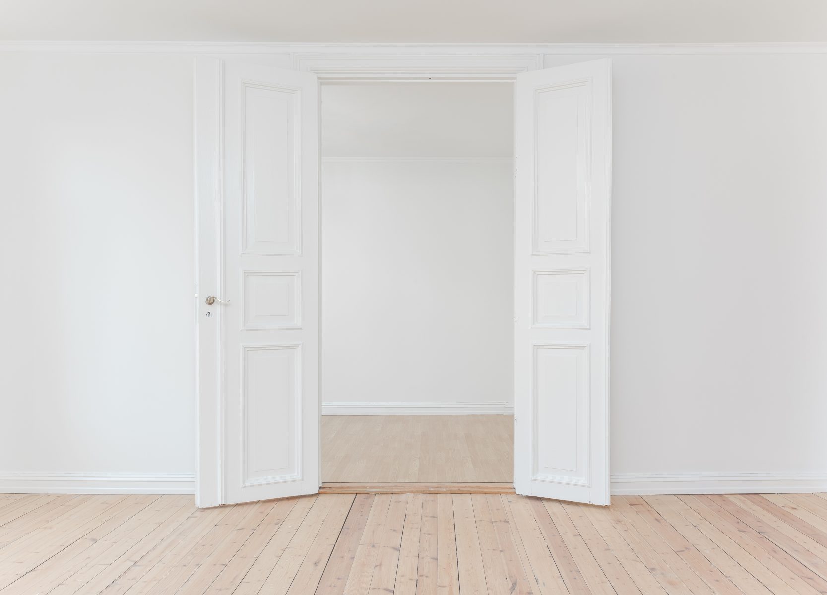 photo of an wide open white door, wood floor and white wall - home renovation tips